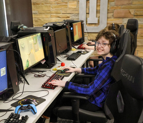 Student sitting in front of computer with headset smiling